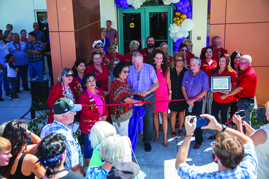 Group of people cutting a red ribbon in front of a new building